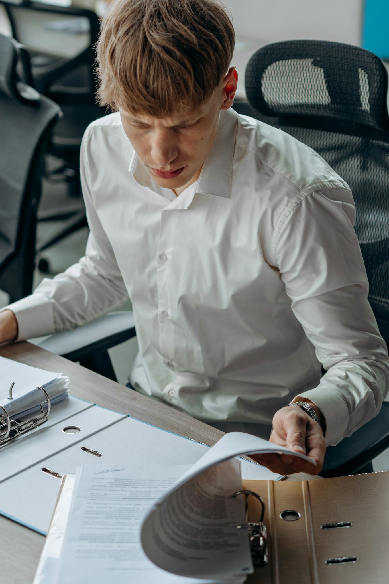 An office worker in a white dress shirt reviewing documents at a desk, emphasizing focus and productivity.